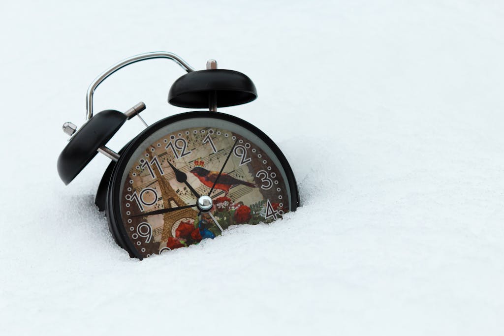 A vintage alarm clock with an Eiffel Tower design partially buried in snow, capturing a winter theme.
