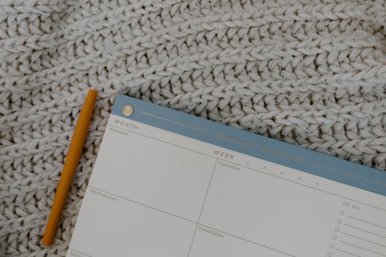 Weekly planner and pen on knitted fabric, perfect for organizing plans and having a productive weekend